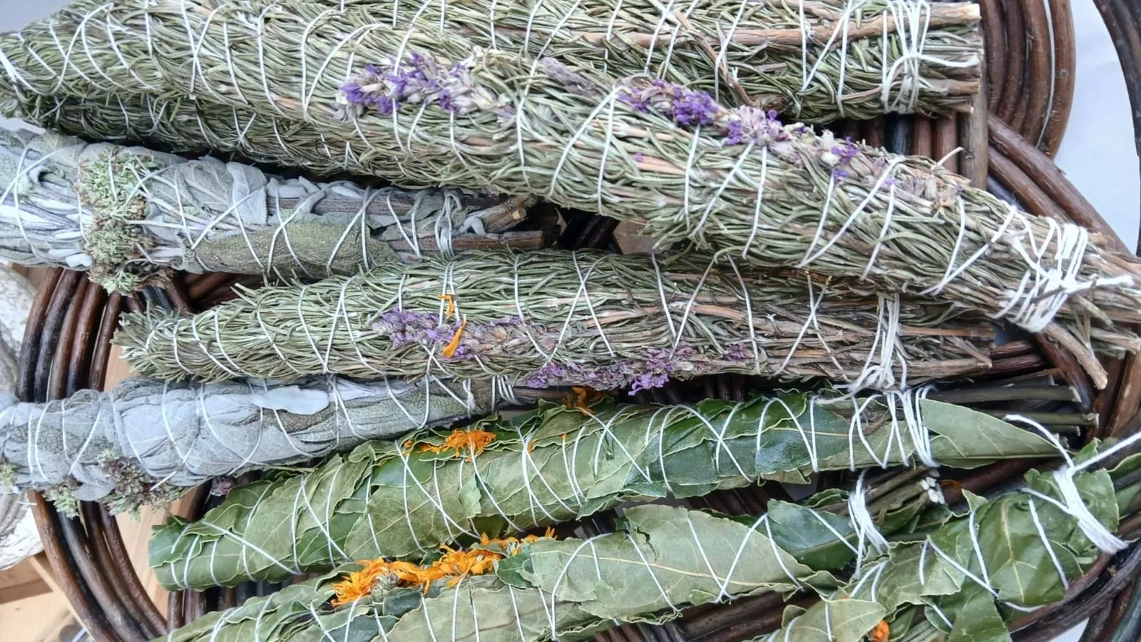 Bâtons de fumigation de feuillage vert, de fleurs violettes et orangées liés au fil blanc, dans une corbeille