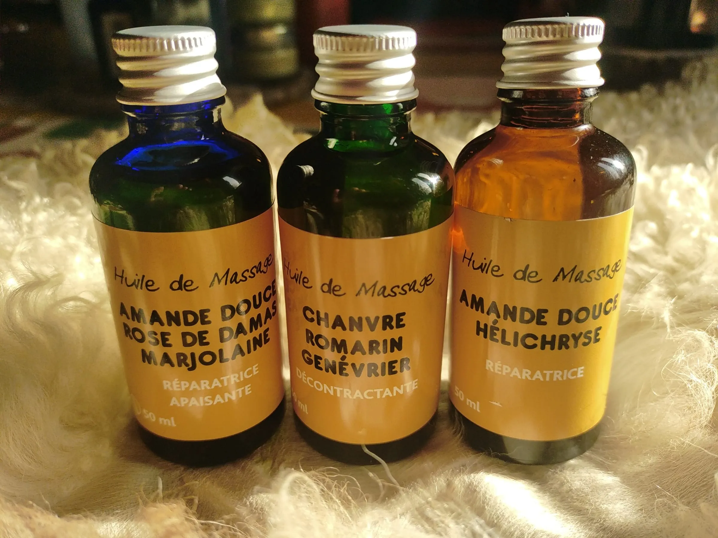 Les trois huiles de massage aux étiquettes jaunes, alignées sur une toison